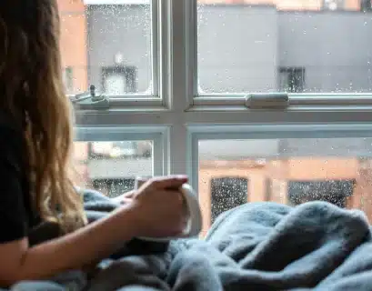 Jeune femme prenant son café devant sa fenêtre alors qu'il fait froid et pleut dehors